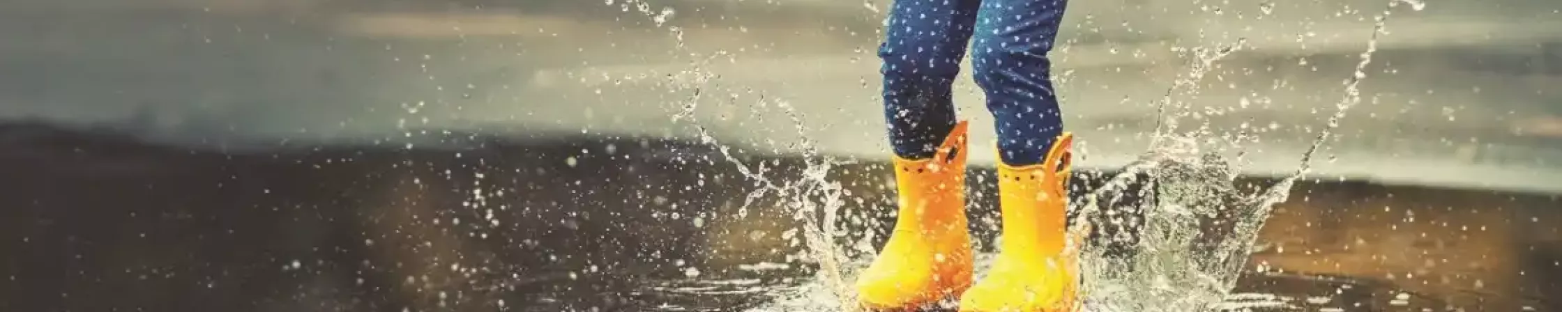 Girl with rubber boots in the rain jumps into a puddle.